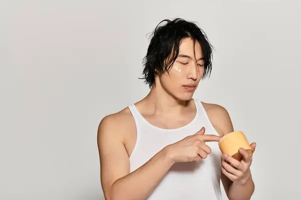 Chic young man focused on skincare routine while dressed casually in a trendy environment. — Stock Photo