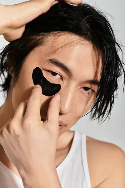 Young man uses a trendy under eye mask, highlighting his skincare routine and youth culture. — Stock Photo