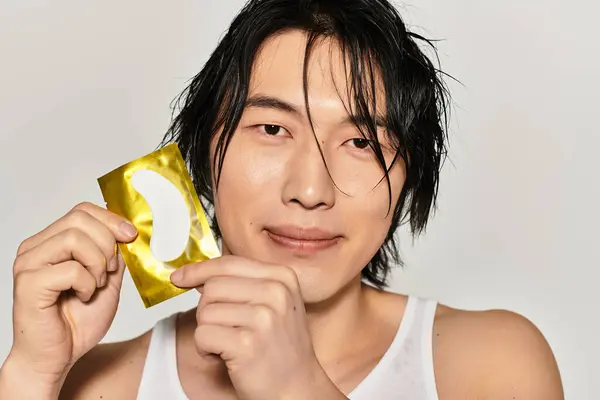 Selbstbewusster junger asiatischer Mann präsentiert ein trendiges Hautpflegeprodukt in einem stilvollen Rahmen. — Stockfoto