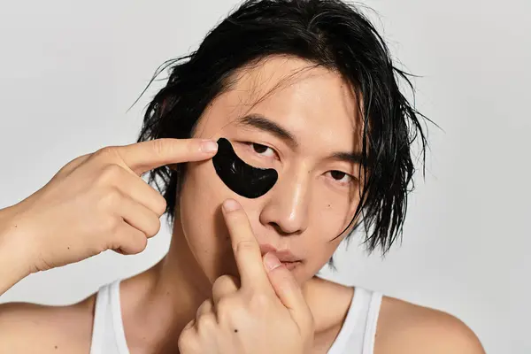 Young, fashionable Asian male engages in modern self care routine with a trendy eye patch. — Stock Photo