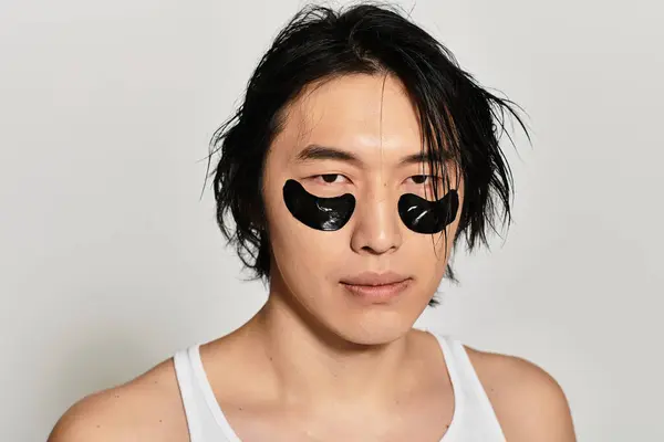 Handsome young Asian male poses confidently in stylish black eye masks, showcasing fashion. — Stock Photo