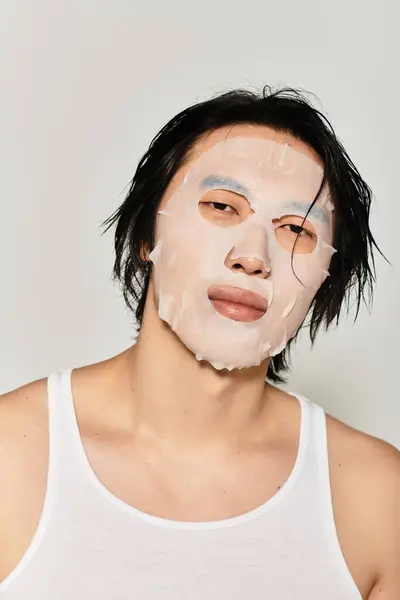 A stylish young Asian male confidently applies a facial mask, embodying youth culture. — Stock Photo