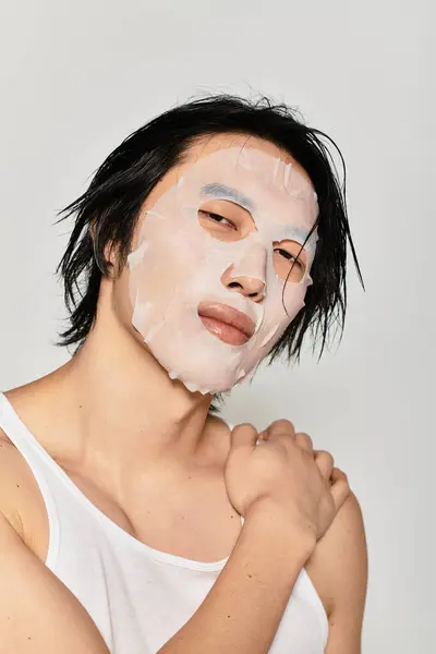 A young man confidently applies a chic facial mask, highlighting his youthful beauty. — Stock Photo