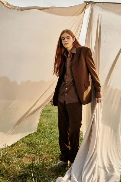 Elegant young man stands confidently in a fashionable outfit, surrounded by soft drapes in nature. — Stock Photo