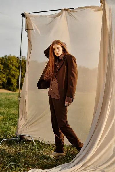 Young man with long hair showcases modern fashion in a serene green landscape during golden hour. — Stock Photo