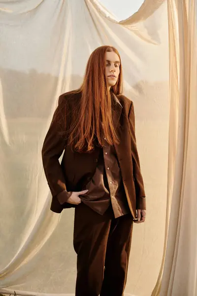 Stylish young man wearing a tailored brown suit stands confidently in a serene environment. — Stock Photo
