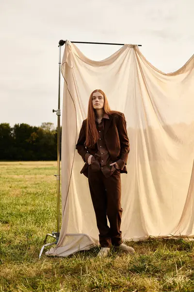 A young man confidently poses in stylish clothes against a soft fabric backdrop at golden hour. — Stock Photo