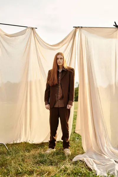A stylish young man confidently poses in a tailored outfit amidst flowing fabric and nature. — Stock Photo
