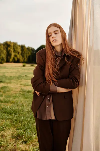 A young handsome man with long hair leans against a curtain in a peaceful grassy field. — Stock Photo