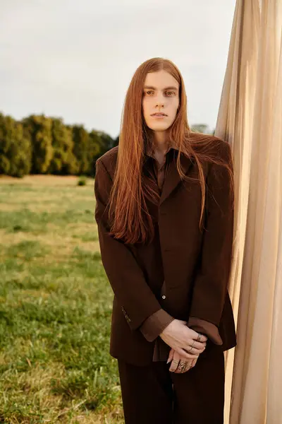 Young man with long hair showcases modern fashion amidst a serene outdoor landscape. — Stock Photo