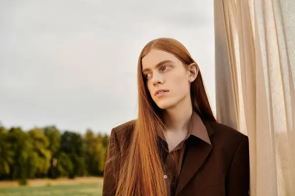 Long haired man showcases fashion sense while leaning against a draped fabric outdoors. — Stock Photo
