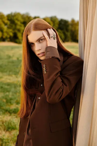 A stylish young man with long hair stands elegantly by a curtain, exuding fashion. — Stock Photo
