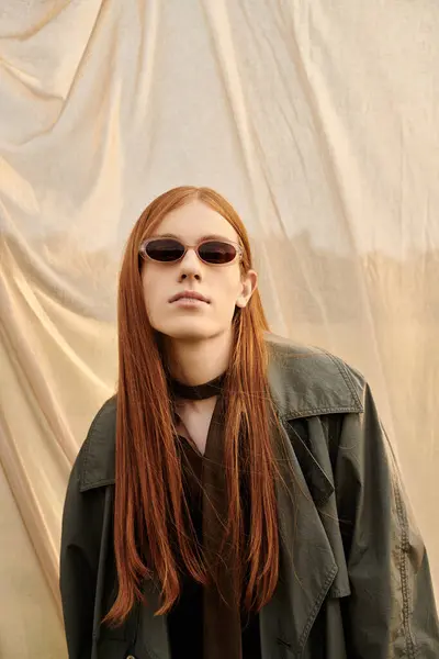 A stylish young man with long hair confidently shows off his fashion against a muted backdrop. — Stock Photo