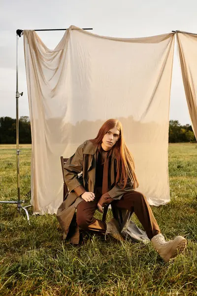 Handsome young man with long hair showcases his unique fashion sense while seated on a chair. — Stock Photo