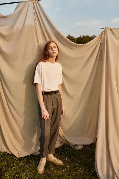 Young man with long hair poses confidently in stylish attire, framed by fabric drapes outdoors. — Stock Photo