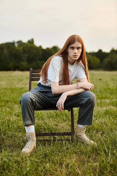A stylish young man with long hair sits in a chair in an open field. — Stock Photo