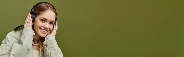 Una donna allegra con un sorriso caldo indossa abbigliamento primaverile alla moda, ascoltando musica con le cuffie. — Foto stock