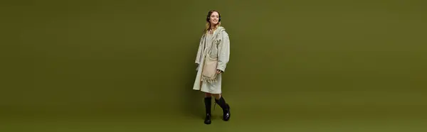 A stylish young woman confidently walks in a trendy spring outfit against a green backdrop. — Stock Photo