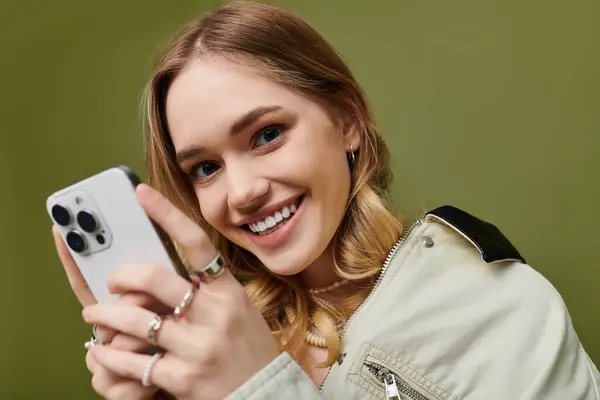 A cheerful young woman in trendy spring clothes happily uses her smartphone. — Stock Photo