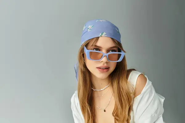 A young woman expresses spring vibes with her trendy outfit and accessories against a grey backdrop. — Stock Photo