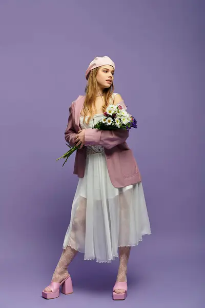 Una joven mujer irradia energía primaveral con su atuendo de moda mientras sostiene flores frescas en un estudio. - foto de stock