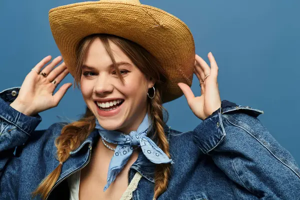 A young woman wearing a denim jacket smiles brightly while adjusting her hat in a lively studio. — Stock Photo