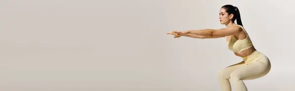Sporty young woman enhances strength and flexibility with focused squats in a bright environment. — Stock Photo