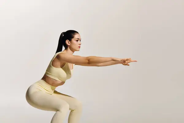 A young sporty woman showcases strength and focus while squatting in a calm setting. — Stock Photo