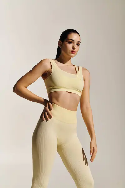 A young, sporty woman confidently showcases her athleticism and style against a soft backdrop. — Stock Photo