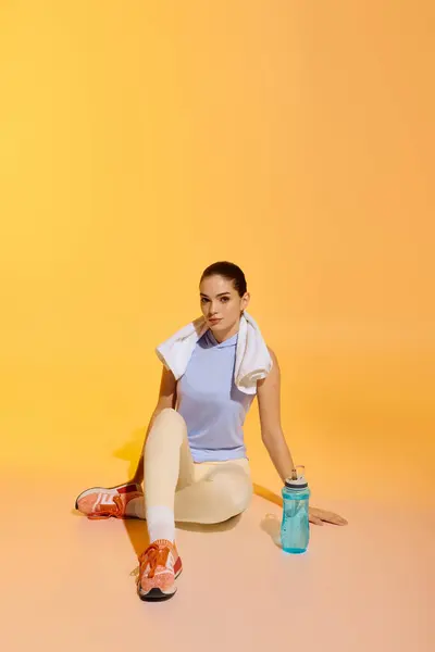A fit woman relaxes on the floor, savoring hydration and post workout calm. — Stock Photo