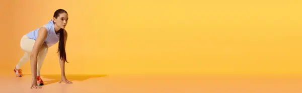 Sporty woman crouching in a dynamic pose, ready to sprint on a bright yellow background. — Stock Photo