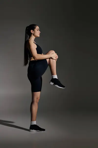 A young sporty woman confidently balances on one leg while stretching in a minimalist gym. — Stock Photo