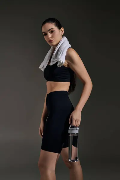 A young, beautiful woman stands confidently with a water bottle and towel around her neck. — Stock Photo