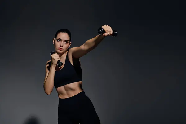 Young woman lifting dumbbells in a dim gym, showcasing agility and dedication. — Stock Photo