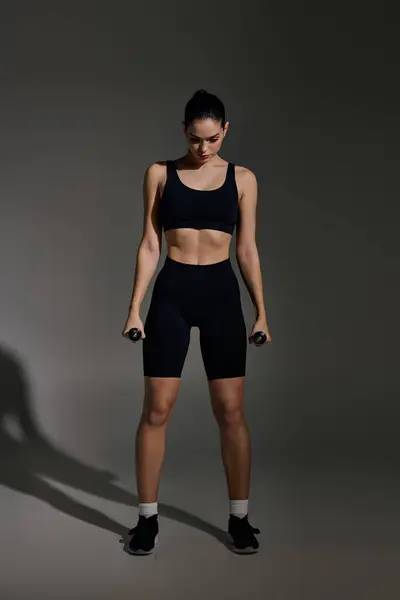 Sporty young woman confidently lifts dumbbells while showcasing her athleticism in a modern space — Stock Photo