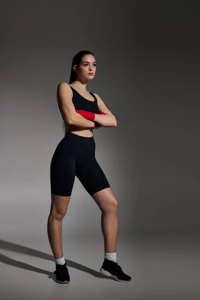 Mujer joven fuerte y hermosa se levanta con confianza con los brazos cruzados en un traje atlético con estilo. - foto de stock
