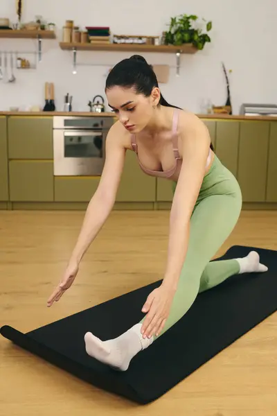 A young woman stretches on a yoga mat in her kitchen, highlighting her athletic figure. — Stock Photo