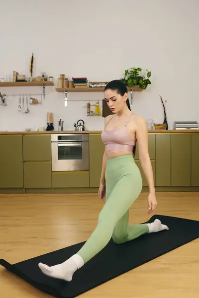 Sportliche Frau macht Yoga-Dehnungen auf einer Matte in einer stilvollen modernen Küche. — Stockfoto