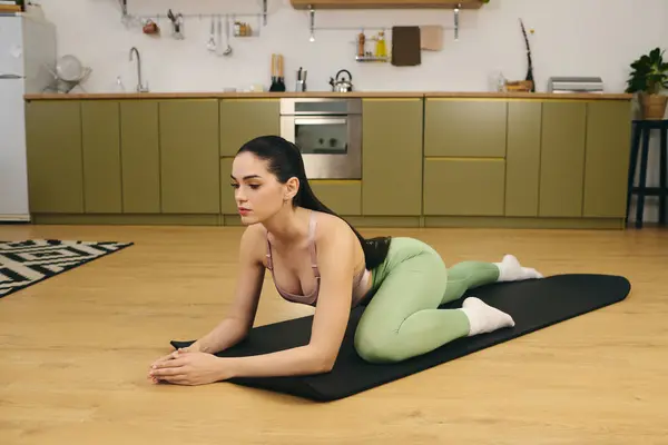 Sporty woman engages in a yoga pose on a mat surrounded by a stylish kitchen decor — Stock Photo