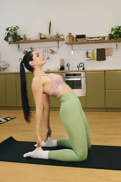 Sporty woman doing yoga on a mat in a stylish kitchen, showcasing her flexibility and focus. — Stock Photo