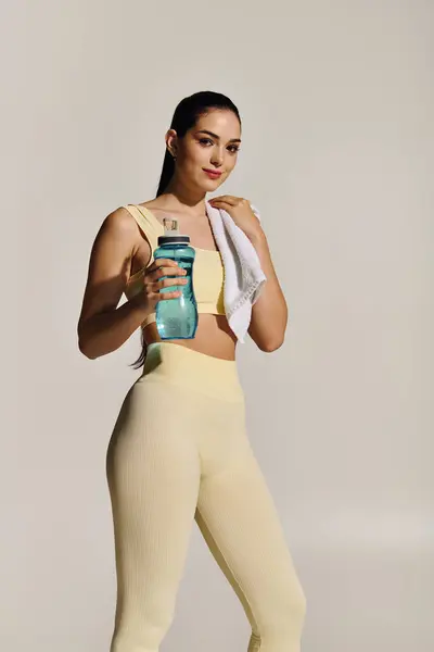 Young woman stands confidently, holding a water bottle and towel, celebrating her fitness routine. — Stock Photo