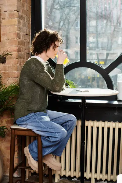 Young man sits by the window sipping a bright drink in a warm and inviting cafe atmosphere. — Stock Photo