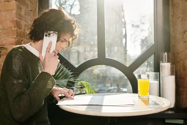 A young man at a cafe examines his menu while sipping a drink and on the phone. — Stock Photo