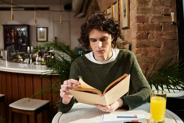 У затишному кафе молодий чоловік читає книгу з освіжаючим напоєм поруч з ним. — стокове фото