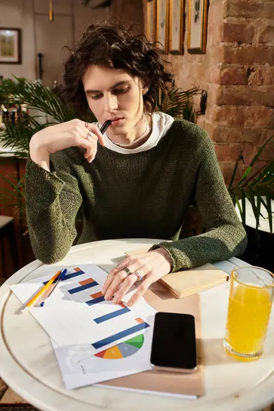 A young man enjoys a drink at a cafe while contemplating colorful charts. — Stock Photo