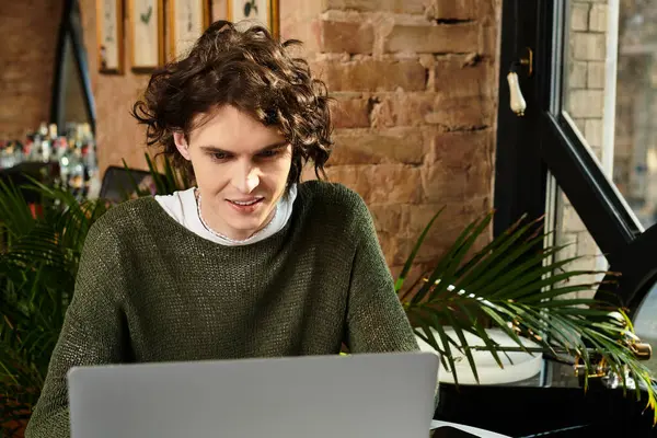 In a vibrant cafe, a handsome young man focuses on his laptop while surrounded by lush plants. — Stock Photo
