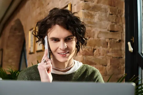 A charming young man at a cozy cafe makes a delightful call while using his laptop. — Stock Photo