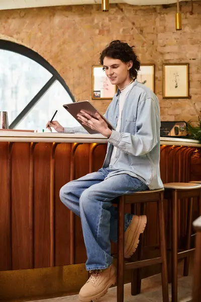A young handsome guy sits at a stylish cafe, focused on writing while sipping coffee. — Stock Photo