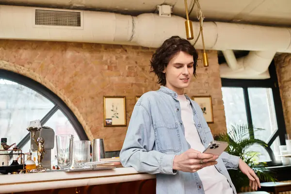 Inside a cozy cafe, a handsome young man sits casually, engaged with his smartphone in hand. — Stock Photo