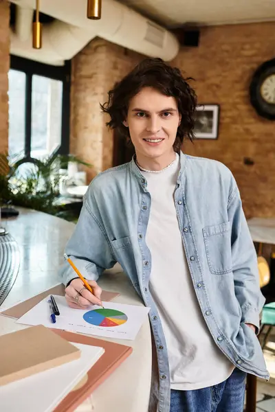 Handsome young guy leans against the counter in a cafe, pen in hand, engaged in a creative task. — Stock Photo